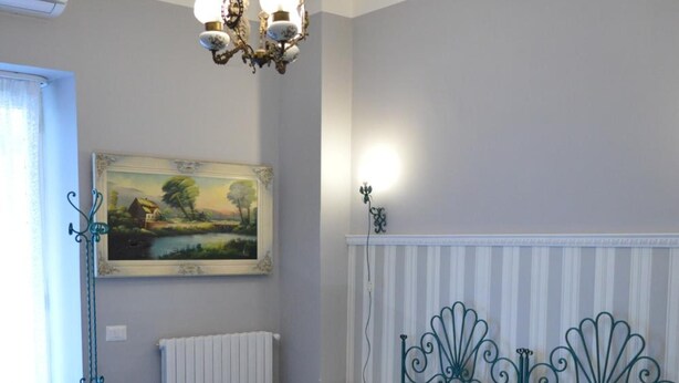 A bedroom with a bed, a radiator, a painting, and a chandelier. - B B Al Golfo (Salerno)