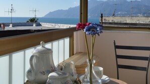 A balcony with a table set for tea, overlooking a beach and mountains. - B B Al Golfo (Salerno)