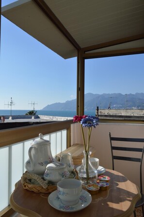 A balcony with a table set for tea, overlooking a beach and mountains. - B B Al Golfo (Salerno)