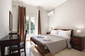 Ein Schlafzimmer mit Bett, Nachttischen, Schreibtisch, Stuhl und einem Fenster mit Vorhängen.