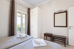 Ein Hotelzimmer mit zwei Betten, einem kleinen Tisch, einer Bank, einem Spiegel und einer Tür zu einem Außenbereich.