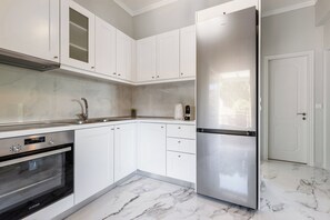 Eine moderne Küche mit weißen Schränken, einem Edelstahl-Kühlschrank, einem Einbauofen und Marmorböden.