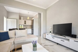 Ein modernes Wohnzimmer mit einer Couch, einem Flachbildfernseher, einem Couchtisch und einer Küche im Hintergrund.