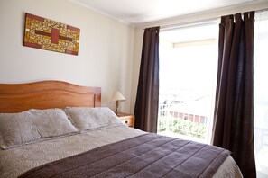 A bedroom with a bed, a nightstand, a lamp, a window with curtains, and a wall art piece. - Hotel Y Cabañas Portal Del Inca (Caldera)