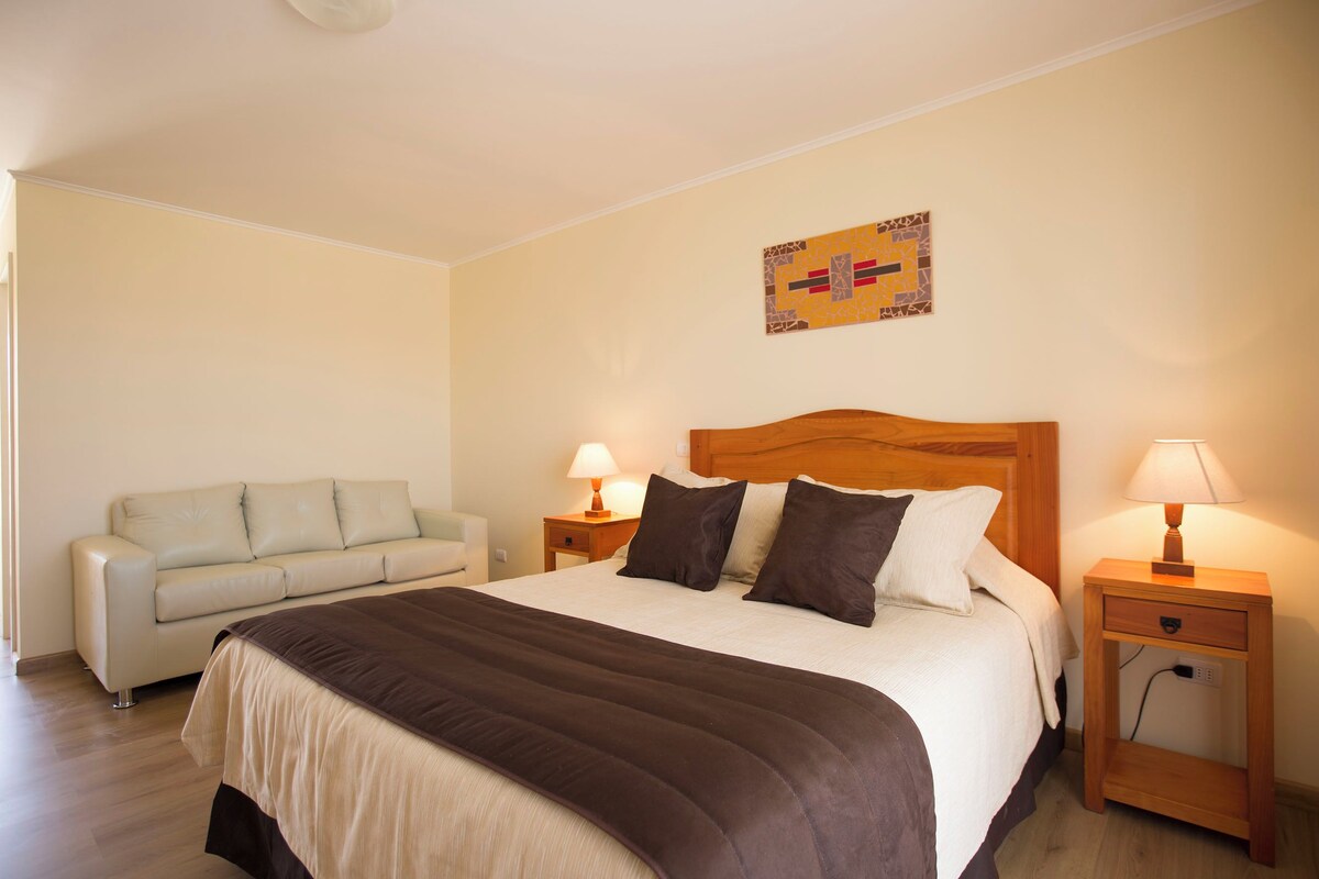 A hotel room with a bed, a sofa, two bedside tables with lamps, and a wall art piece.