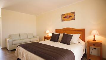 A hotel room with a bed, a sofa, two bedside tables with lamps, and a wall art piece.