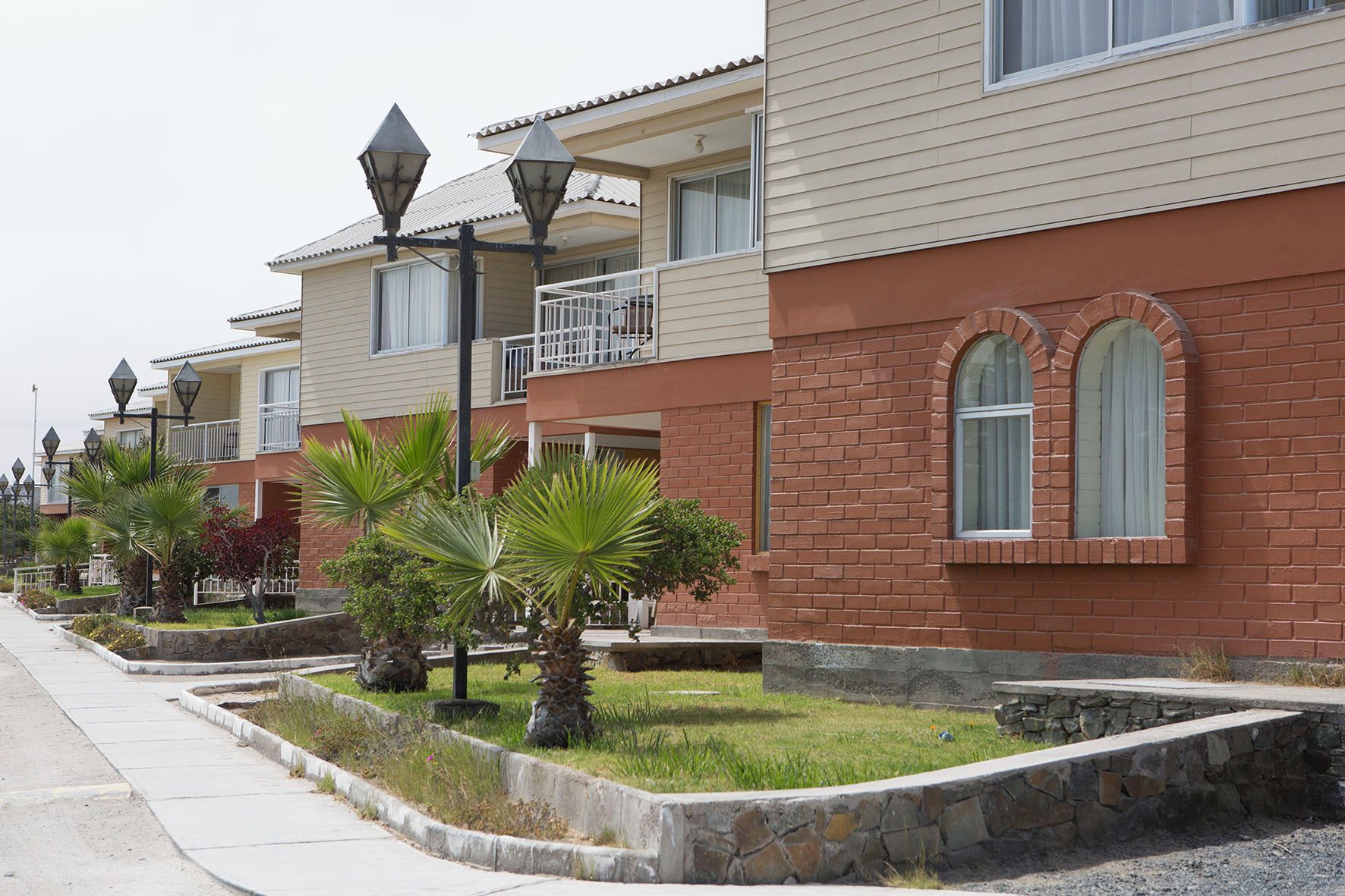 Una hilera de edificios residenciales con balcones, farolas y un muro de piedra con vegetación.
