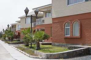 A row of residential buildings with balconies, street lamps, and a stone retaining wall with greenery. - Hotel Y Cabañas Portal Del Inca (Caldera)