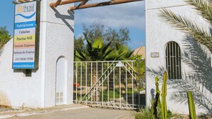 Un edificio blanco con un arco de madera, un cartel que enumera los servicios y un cactus al frente.