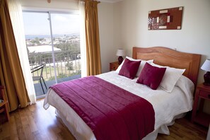 A hotel room with a large bed, a balcony with a view, a wooden headboard, and a nightstand with a lamp. - Hotel Y Cabañas Portal Del Inca (Caldera)