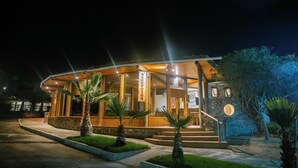 Una reception d'hotel con facciata in pietra, rivestimento in legno e palme sullo sfondo.