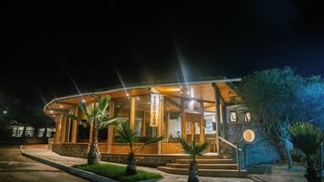 A hotel reception with a stone facade, wooden exterior, and palm trees in the foreground.