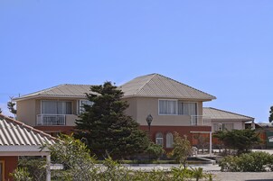 Un edificio residencial de dos plantas con techo inclinado, balcón y un pequeño jardín.