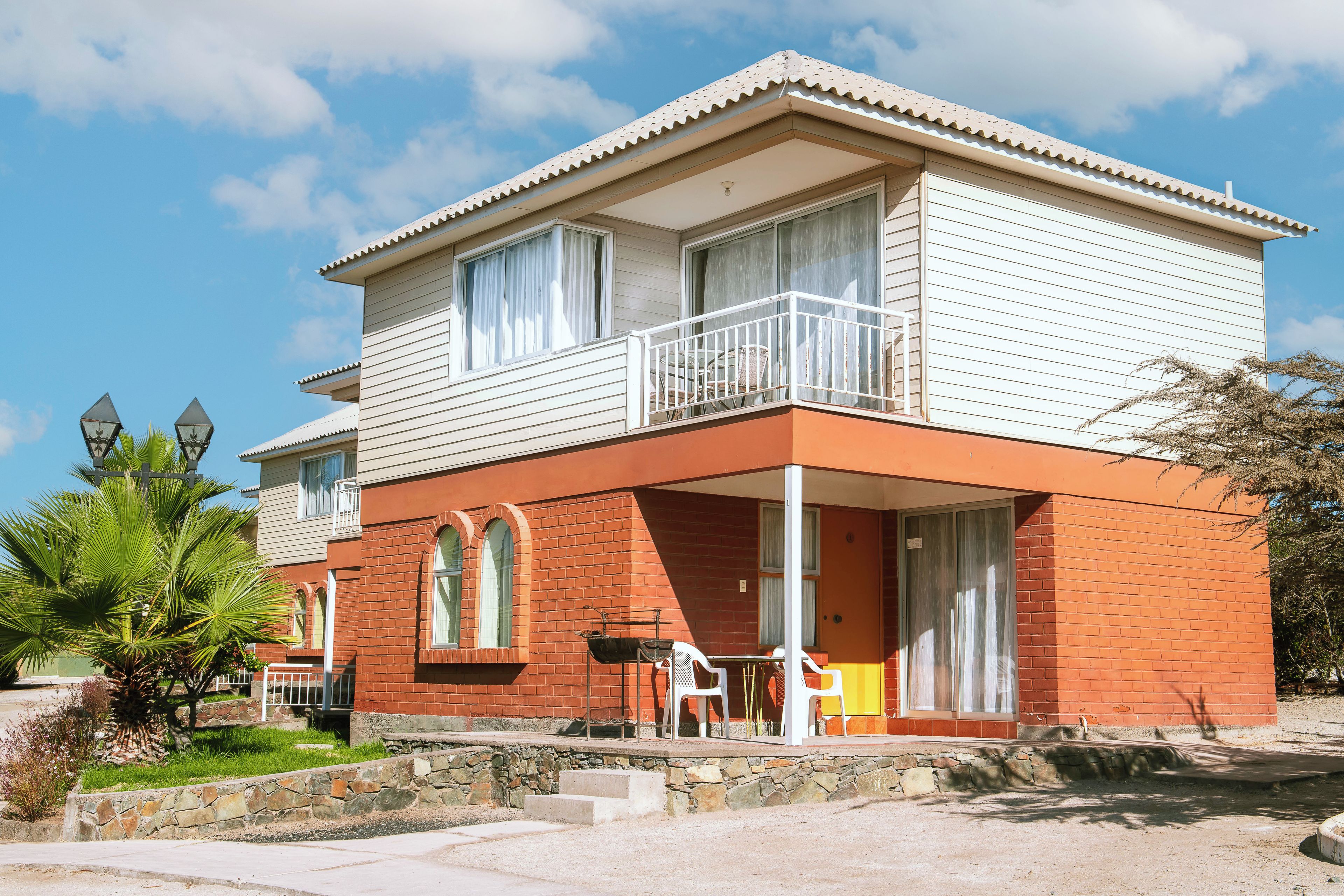 A two-story building with a balcony, a patio with chairs, and a stone wall.