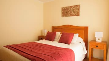 A neatly made bed with a red blanket, a wooden headboard, and a bedside table with a lamp.