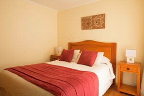 A neatly made bed with a red blanket, a wooden headboard, and a bedside table with a lamp. - Hotel Y Cabañas Portal Del Inca (Caldera)