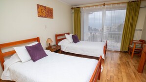 Habitación de hotel con dos camas de madera, una mesita de noche, una silla y vistas amplias por un ventanal.