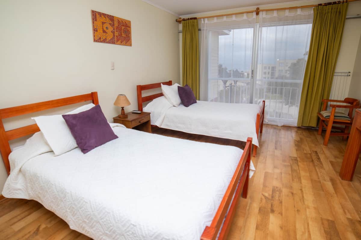 A hotel room with two wooden beds, a nightstand, a chair, and a view through a large window.