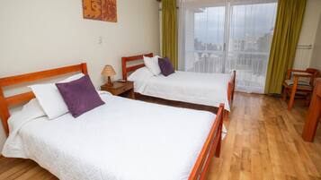 A hotel room with two wooden beds, a nightstand, a chair, and a view through a large window.
