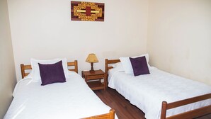 Una habitación con dos camas de madera, ropa de cama blanca y una mesita de noche con lámpara.