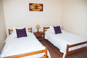 A room with two wooden beds, white bedding, and a small bedside table with a lamp.