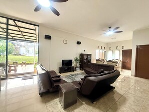 A spacious living room with a large TV, comfortable seating, and a sliding glass door leading to a patio. - Sf Homey Galaxy Resort (Cipanas)