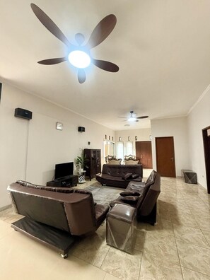 A spacious living room with a large sectional sofa, a television, and a ceiling fan. - Sf Homey Galaxy Resort (Cipanas)