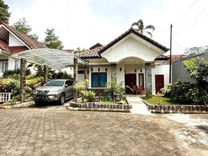 A residential house with a covered driveway, a parked car, and a well-maintained garden. - Sf Homey Galaxy Resort (Cipanas)