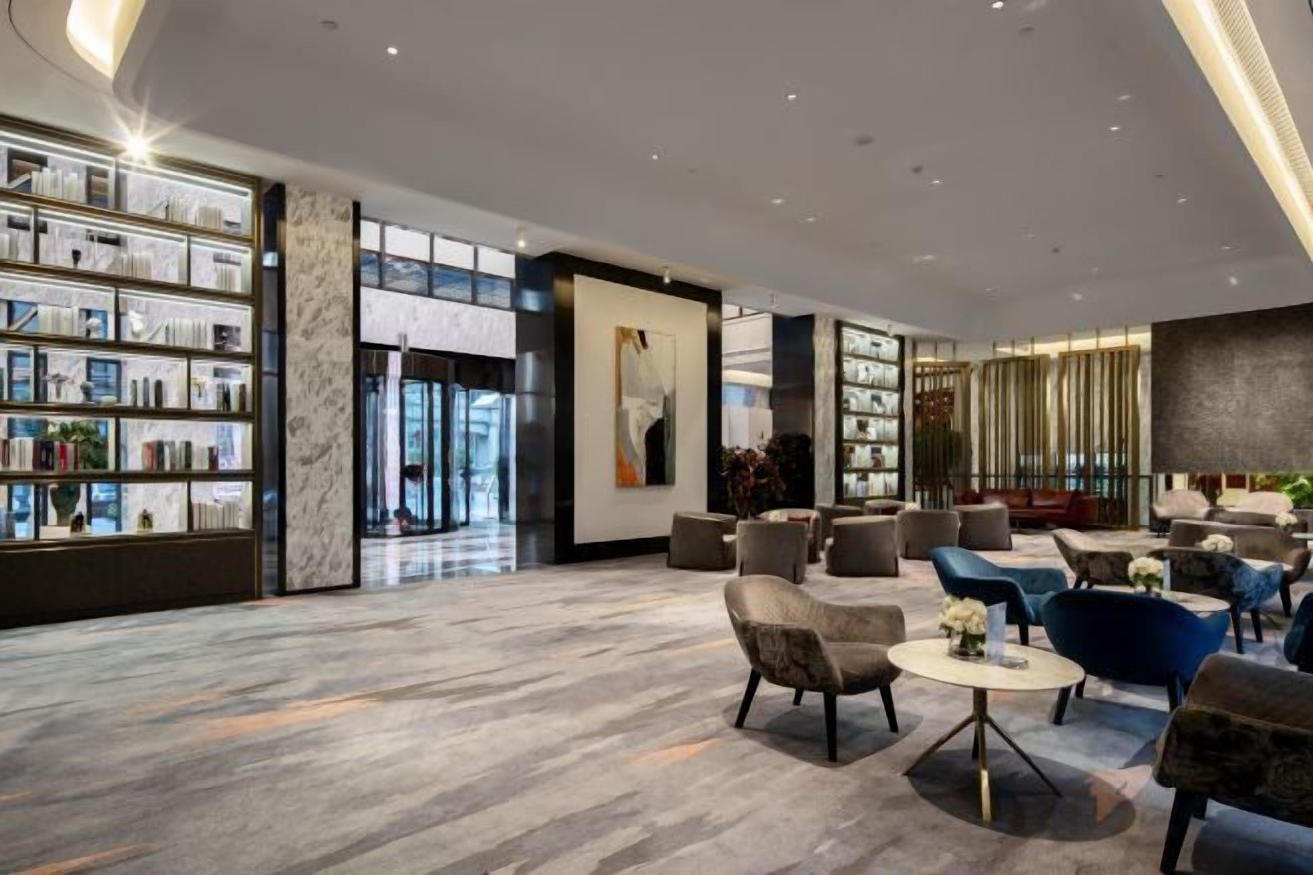 A modern lobby with a marble floor, seating area with sofas and chairs, and a bookshelf.
