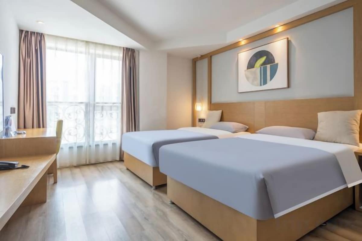 A hotel room with two beds, a desk, and a window with curtains.