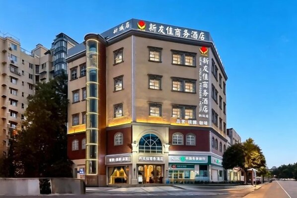 A multi-story hotel with a prominent sign at the top, large windows on the facade, and a ground-level entrance with signage. - Youjia Traders Hotel (Pengzhou Longxing Temple) (Chengdu)