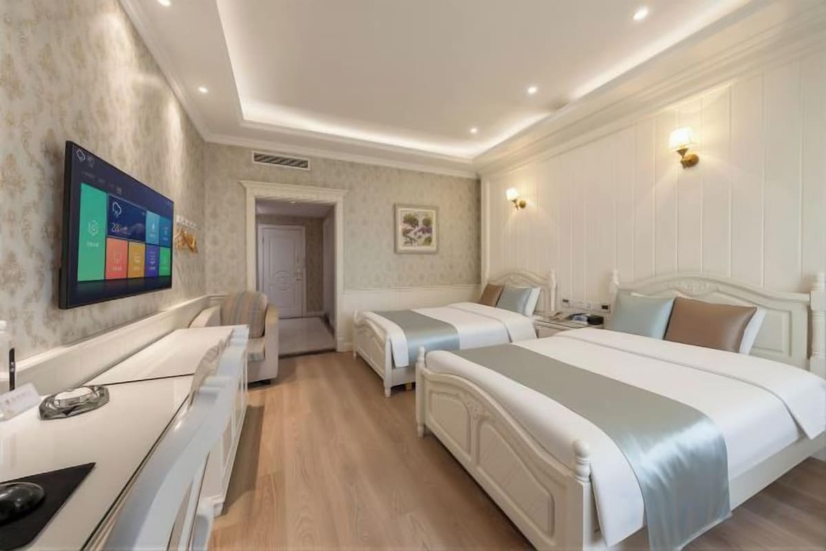 A hotel room with two beds, a desk, and a flat-screen TV mounted on the wall.