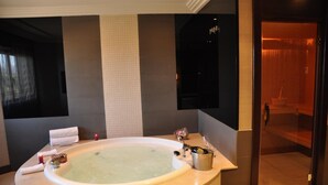 Een moderne badkamer met een vrijstaand bad, een spiegel en een houten deur naar een sauna.