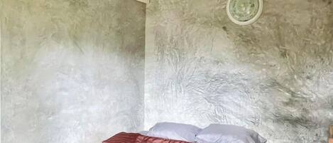 Una habitación con una cama, aire acondicionado en la pared y una lámpara circular.