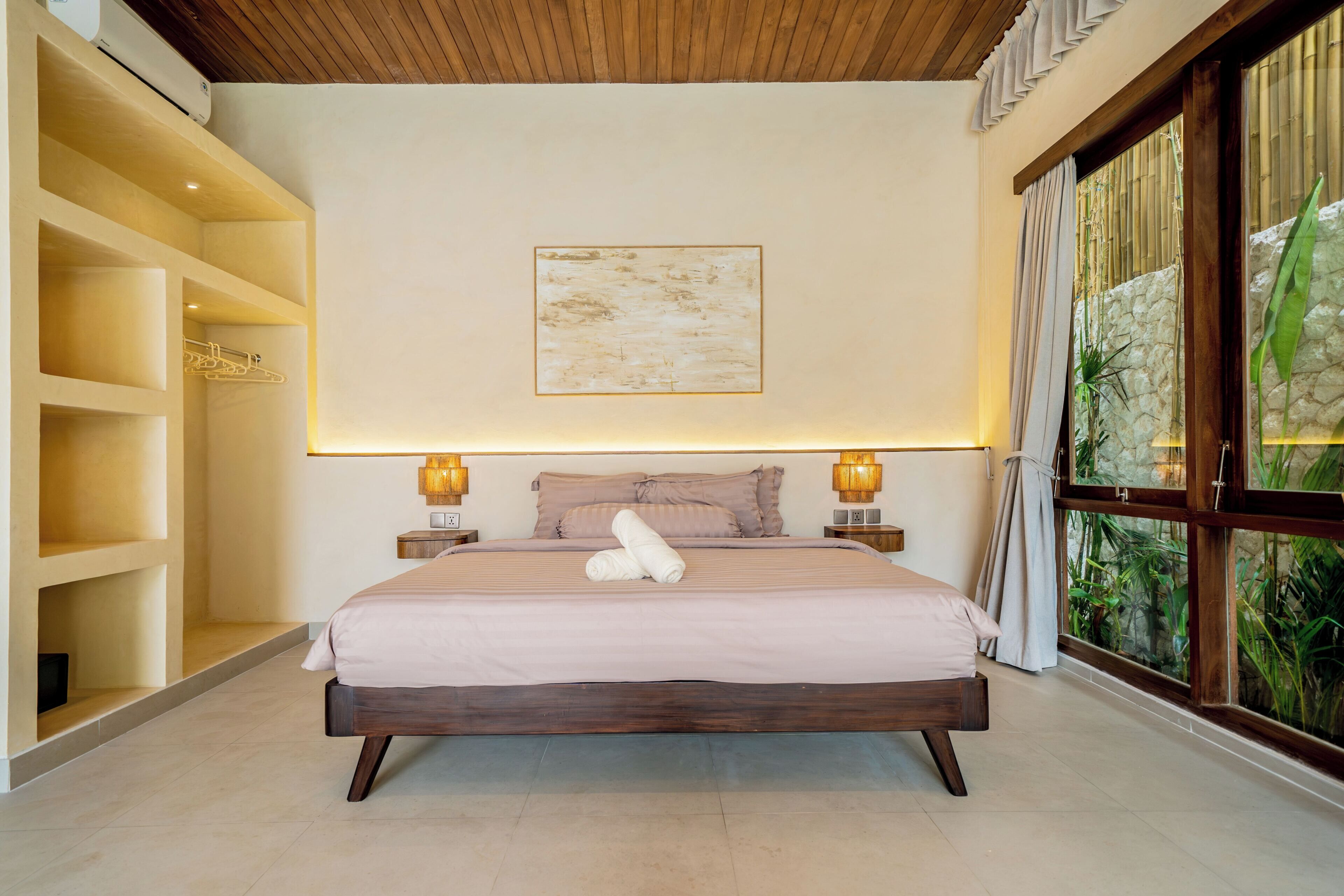 A bedroom with a large bed, bedside lamps, a wall-mounted artwork, and a view through a window.
