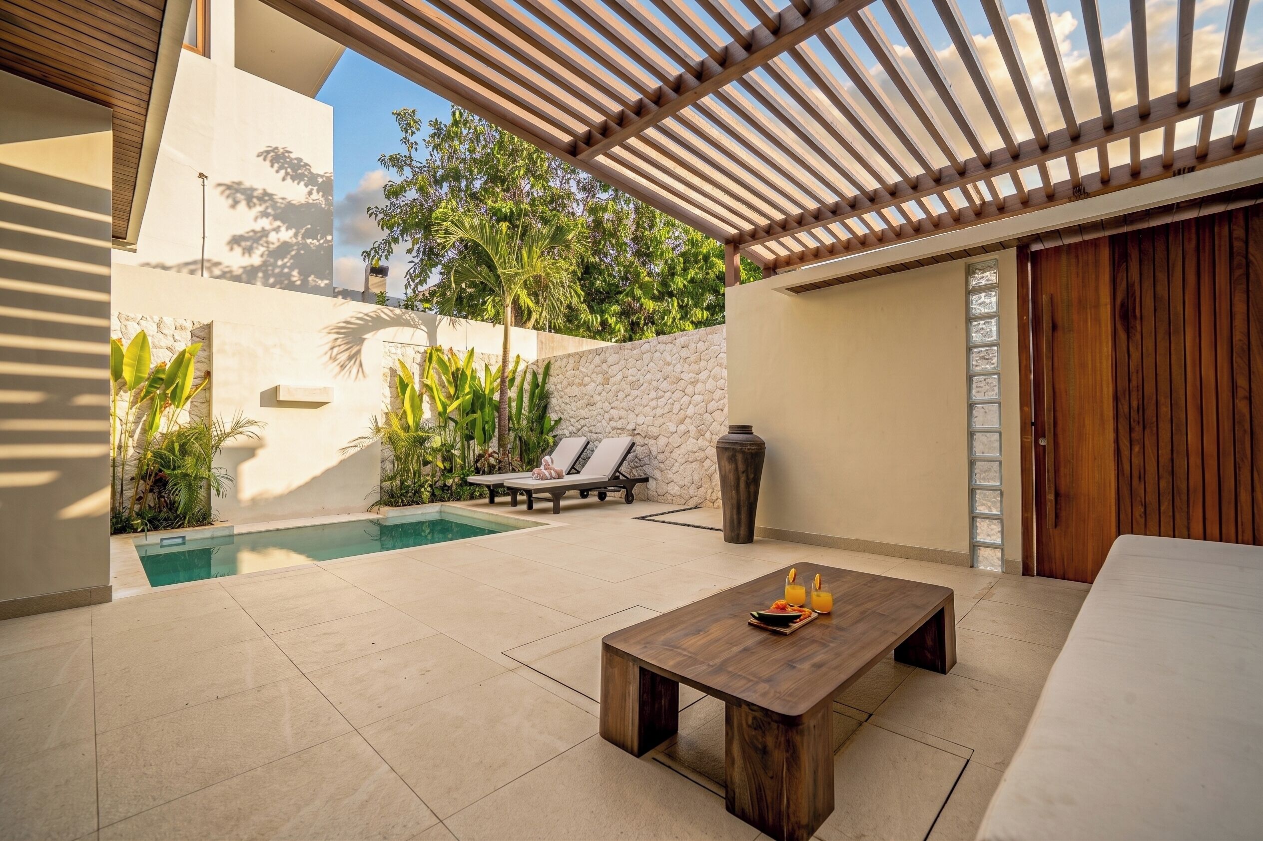 A modern outdoor patio with a pool, lounge chairs, and a wooden table.