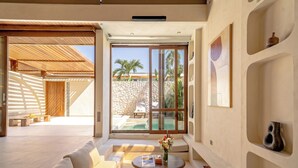 A modern interior with a sofa, coffee table, and a view of a pool and palm trees. - Aozora Villas Uluwatu (Uluwatu)