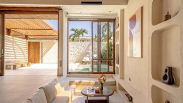 Interior moderno com sofá, mesa de centro e vista para uma piscina e palmeiras.