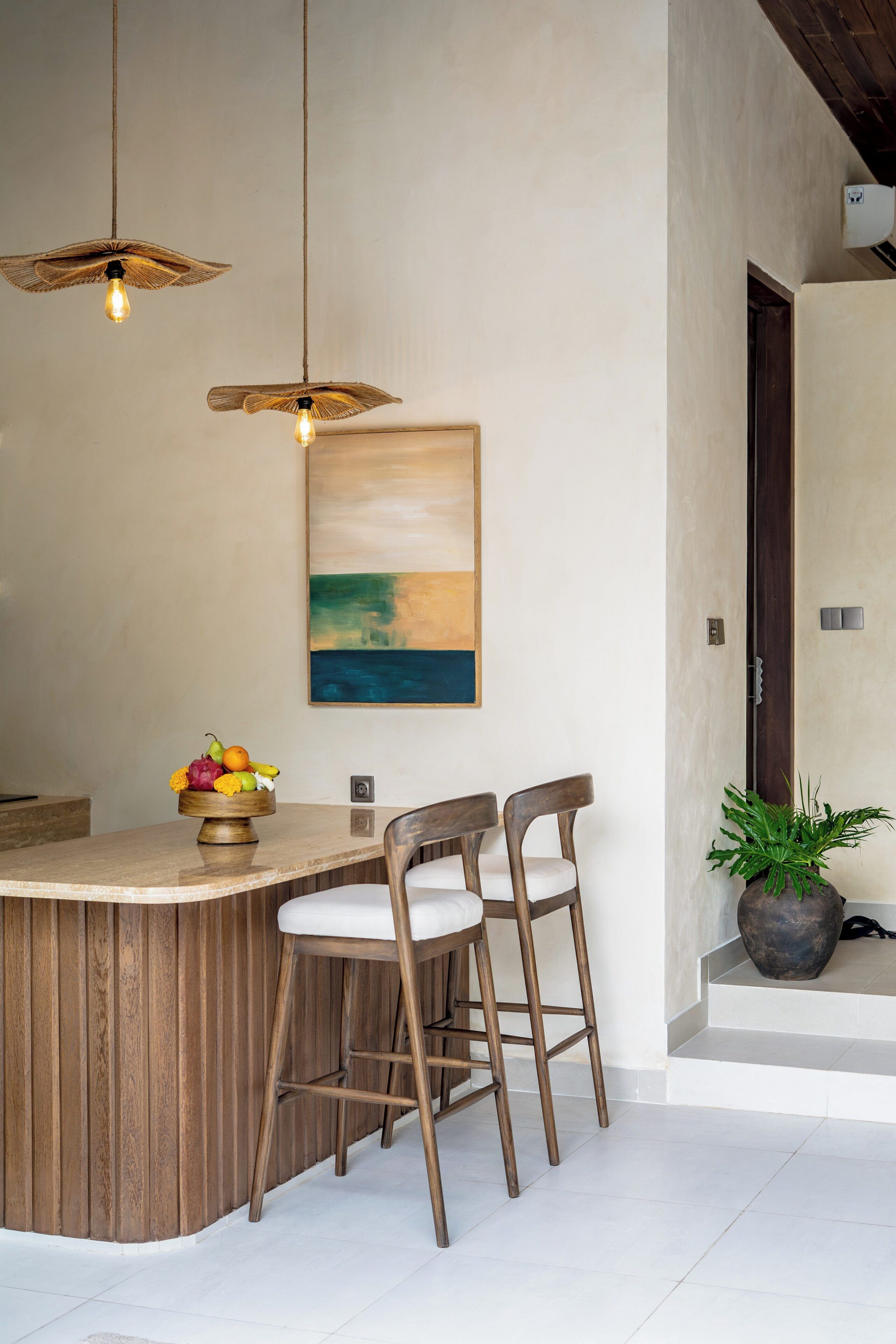 A modern kitchen with a wooden island, two bar stools, pendant lights, and a painting on the wall.