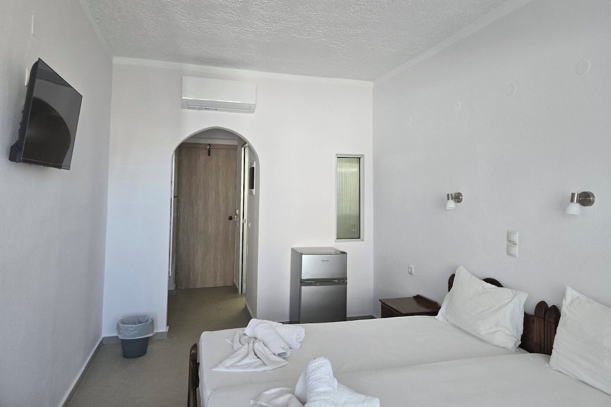 Hotellihuone, jossa on sänky, pieni työpöytä, peili, televisio ja ovi, joka johtaa käytävään.