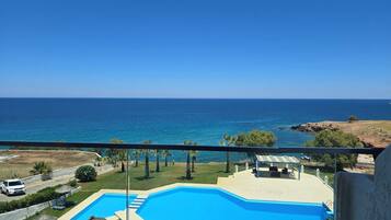 Una piscina con vistas despejadas al mar, una zona ajardinada con árboles y un coche blanco estacionado cerca.