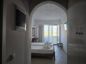 A hotel room with a bed, a small table, a mirror, and a window with curtains. - Stella Beach Hotel Panormos (Mylopotamos)