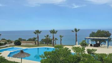 Una piscina con vistas al mar, rodeada de vegetación y una zona de estar con sombra.