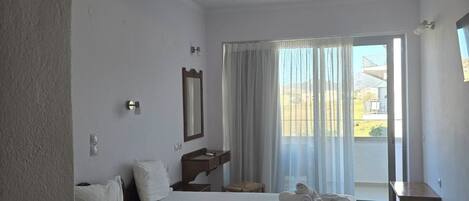 Habitación de hotel con dos camas, una mesita, un espejo y vistas al exterior.