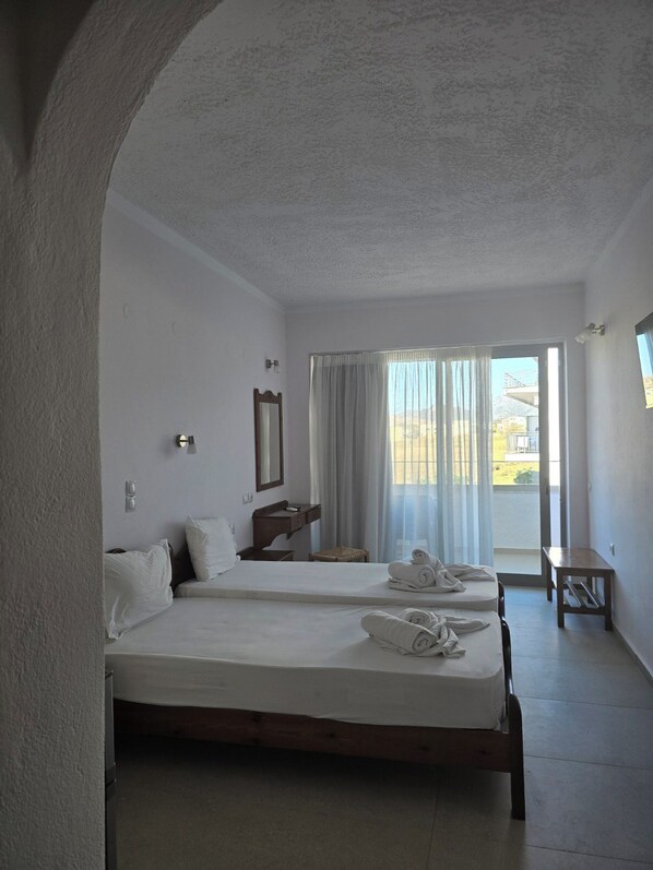 Ein Hotelzimmer mit zwei Betten, einem kleinen Tisch, einem Spiegel und Blick ins Freie.