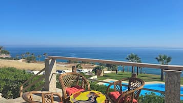 Une terrasse dotée de chaises et d’une table en osier, offrant une vue sur une piscine et l’océan.