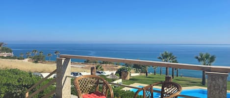Una terraza con sillas de mimbre y una mesa, con vista a una piscina y el océano.