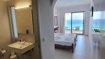 Habitación de hotel con baño, cama, balcón con vista al mar y escritorio.