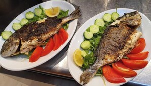 Two plates of grilled fish with vegetables.
