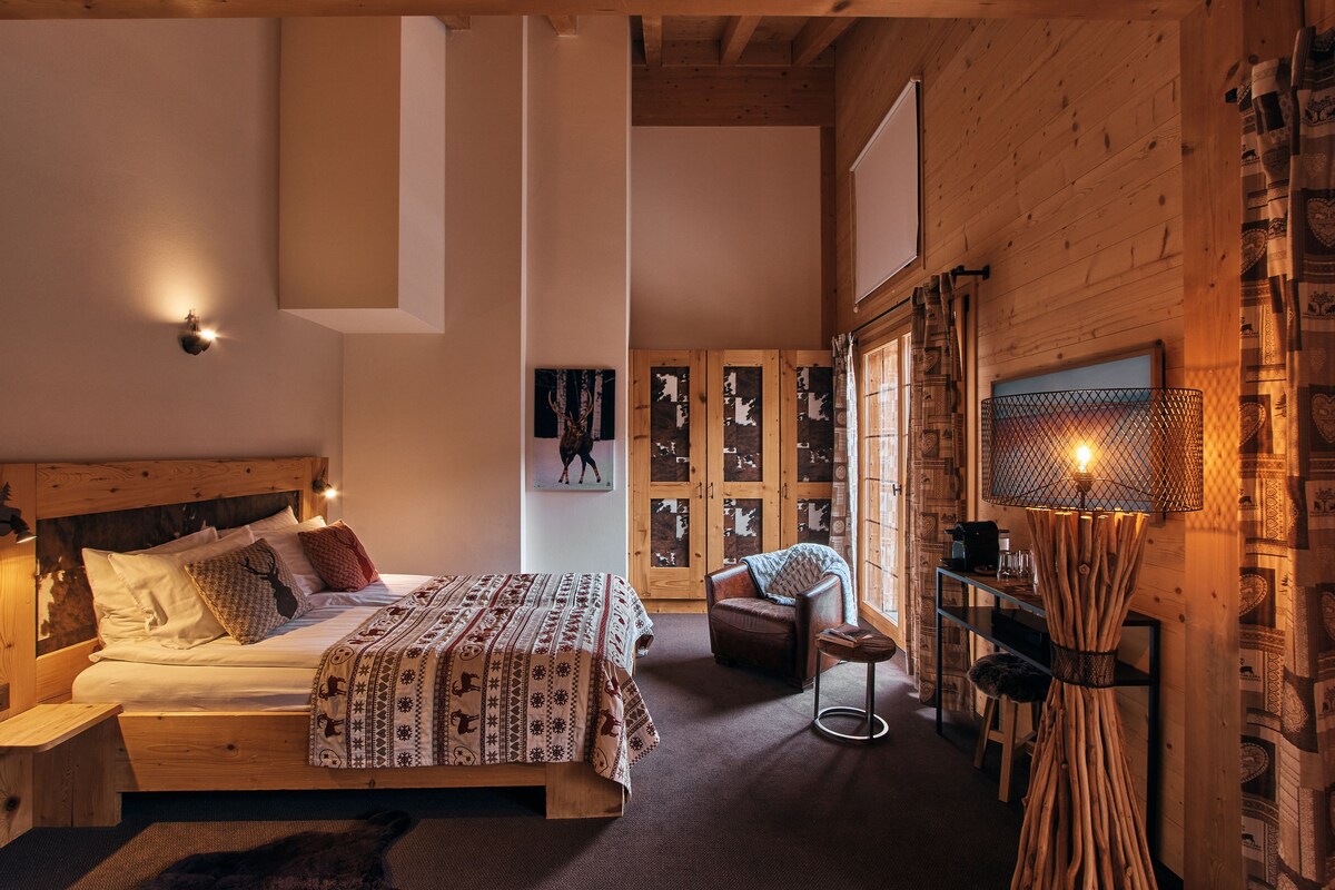 Una habitación de madera con una cama, una silla, una mesa y una lámpara fijada a la pared.